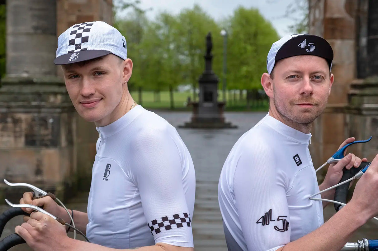 Two cyclists wearing the 45th Anniversary Short Sleeve Mens Jersey by Billy Bilsland Cycles, featuring a white-to-black gradient and checkered sleeve design.