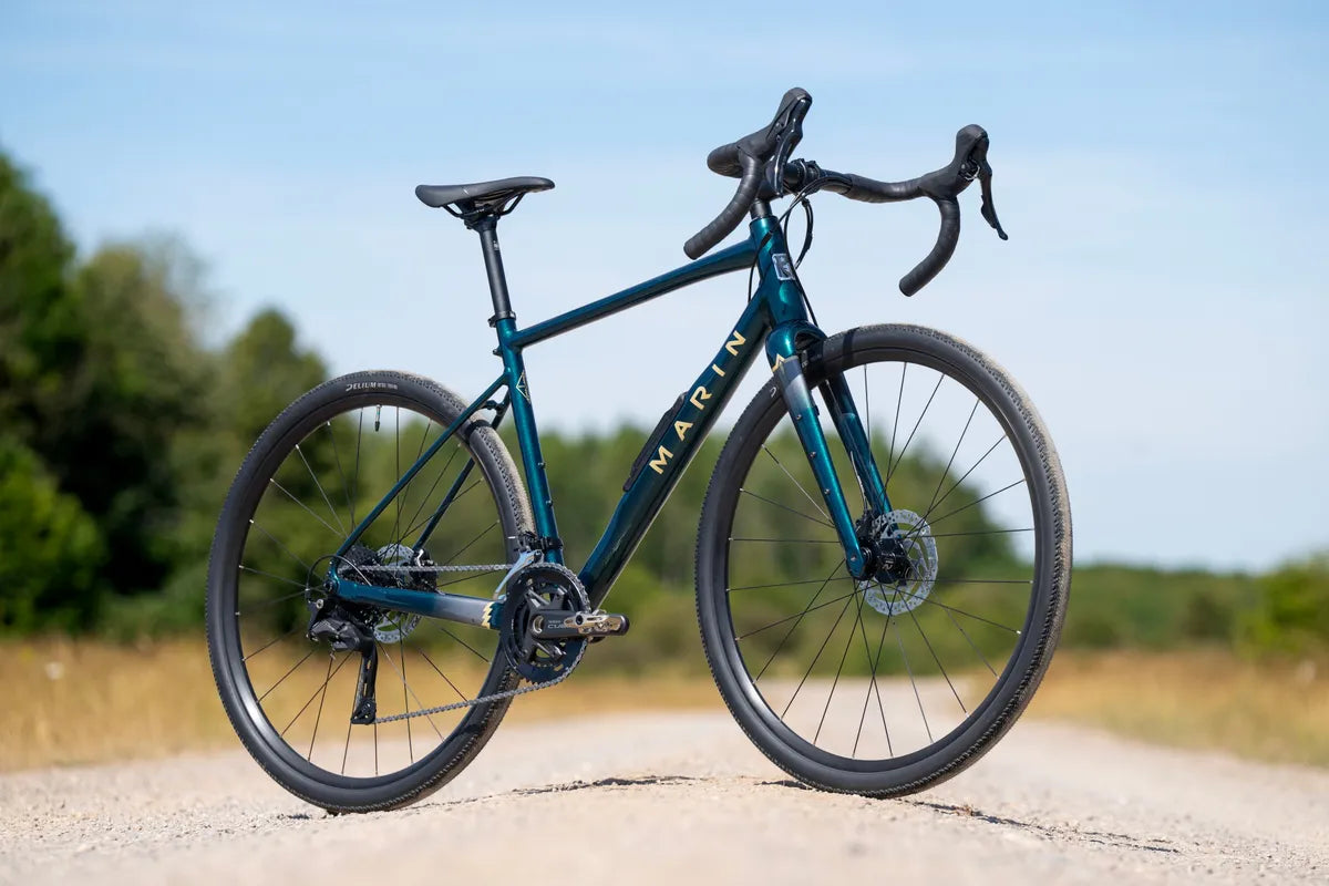 Marin Gestalt 1 gravel bike side-on on a gravel track, with trees and open ground behind