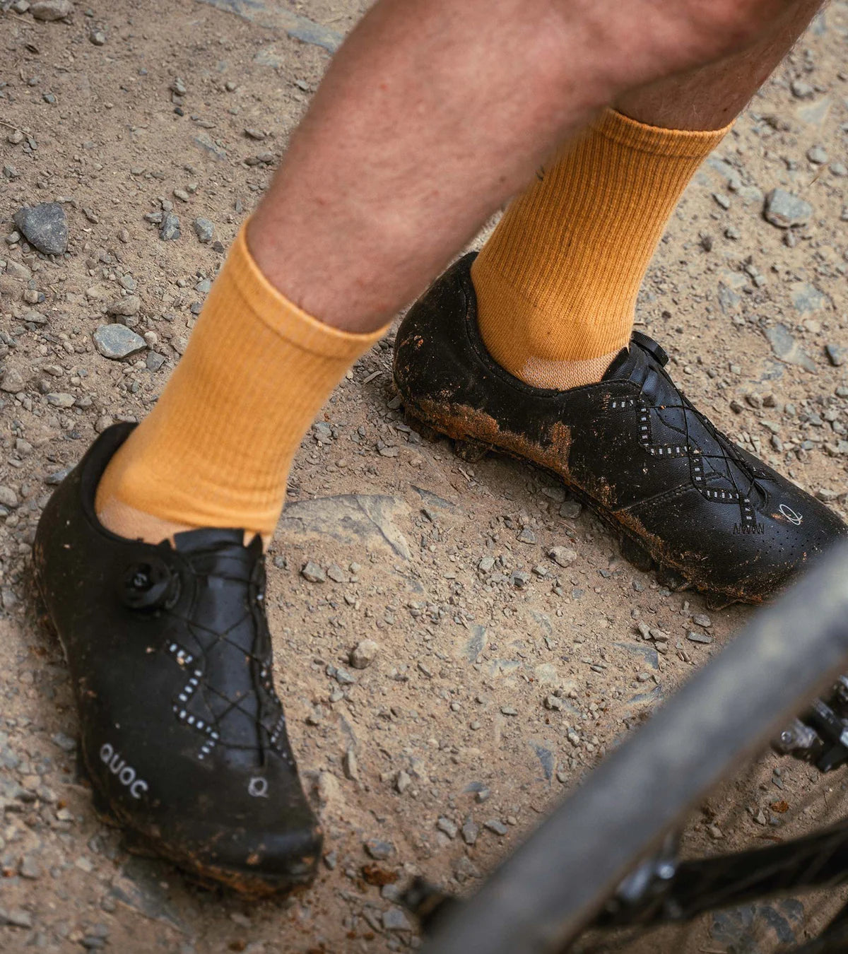 QUOC Escape Off-Road Shoe in black with mud splatter, worn during a gravel ride, showcasing trail-readiness and durability.