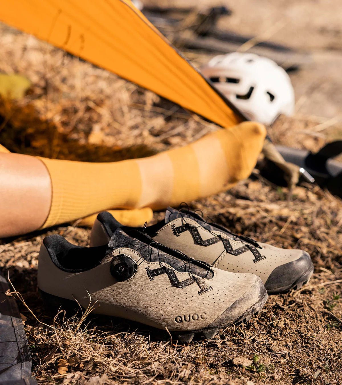 QUOC Escape Off-Road Shoe in sand color resting on dry grass, ideal for rugged outdoor cycling and adventure riding.