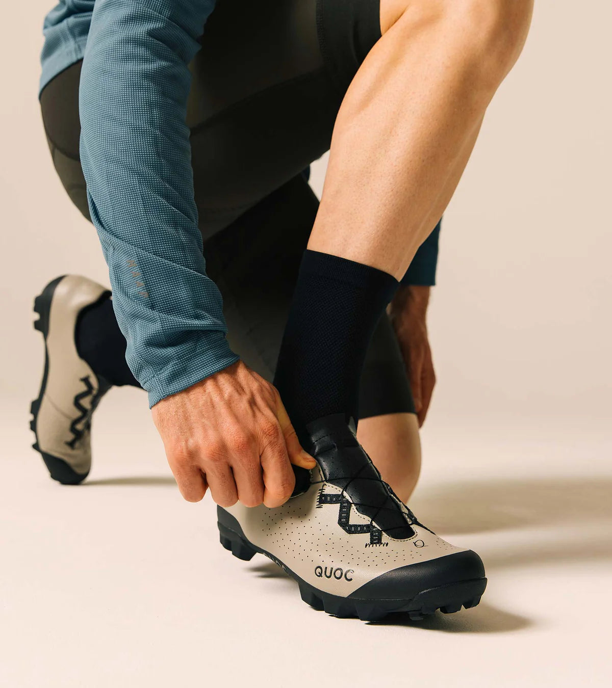 Cyclist adjusting QUOC Escape Off-Road Shoe in sand color, showing ergonomic fit and adventure-ready design.