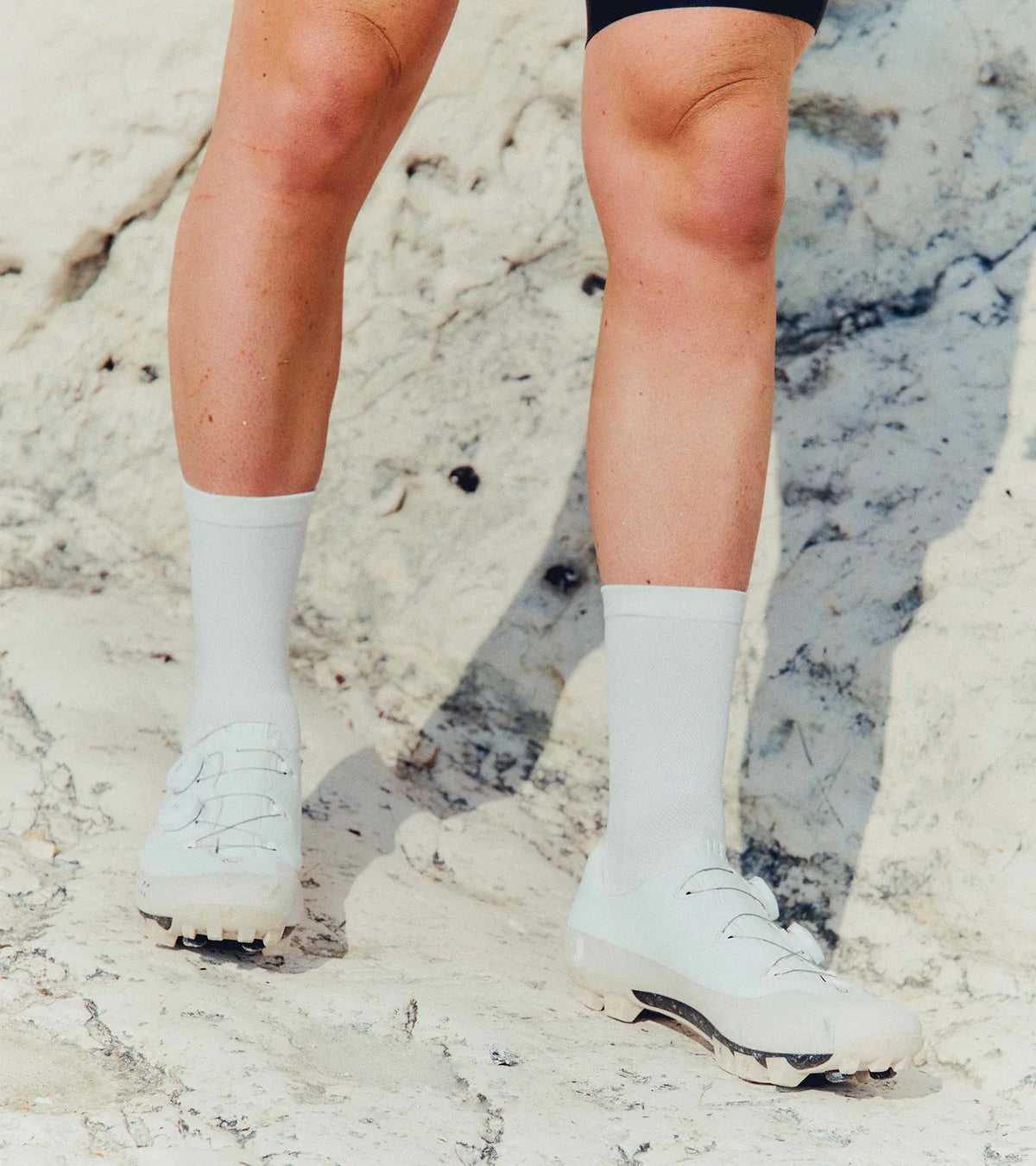 Cyclist wearing QUOC Gran Tourer XC Off-Road Shoes in white, riding on rocky terrain, showcasing their adventure-ready build.