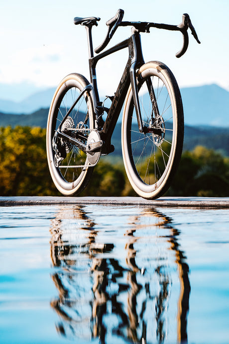 Cervelo Aspero-5 SRAM Force AXS 1 Gravel Bike reflected in water with mountain backdrop, emphasizing its premium design and adventure appeal.