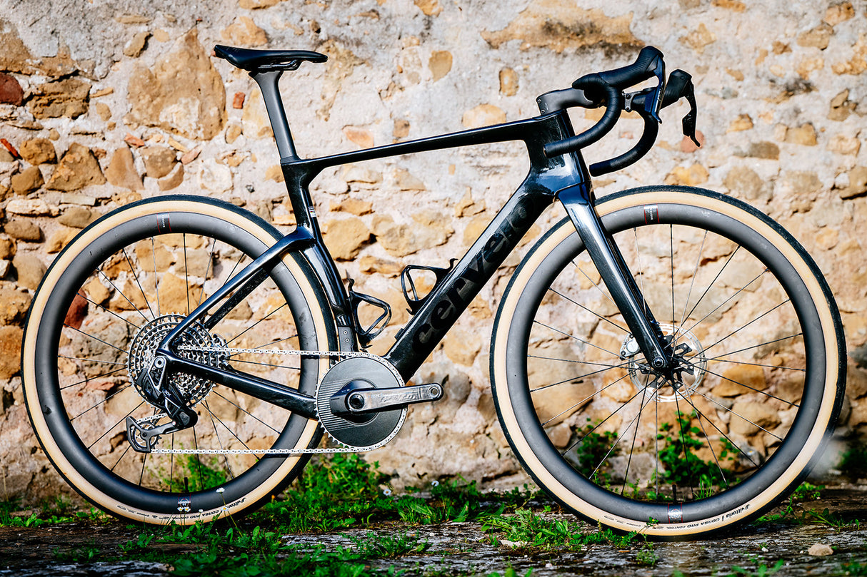 Black Cervelo Aspero-5 SRAM Force AXS 1 Gravel Bike against stone wall, showcasing aerodynamic frame and SRAM Force AXS groupset.