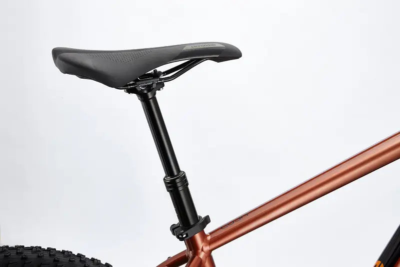 A close-up view of the Cannondale Cujo 1 Kids Mountain Bike highlights its black seat and copper-colored frame. The seat post is adjustable for comfort, and the large, knobby tires are perfect for off-road adventures. The bike is set against a plain white background.
