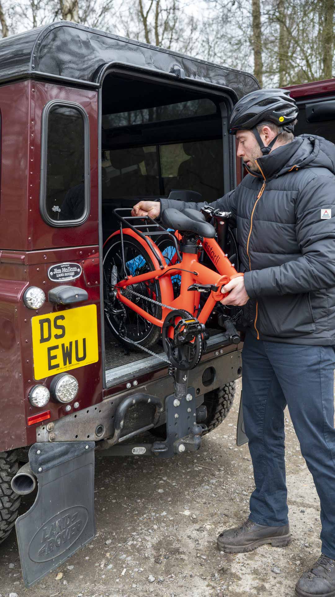 Man loading folded orange estarli E20.7 Comfort Hybrid E-Bike into SUV, highlighting its compact portability for travel and storage.