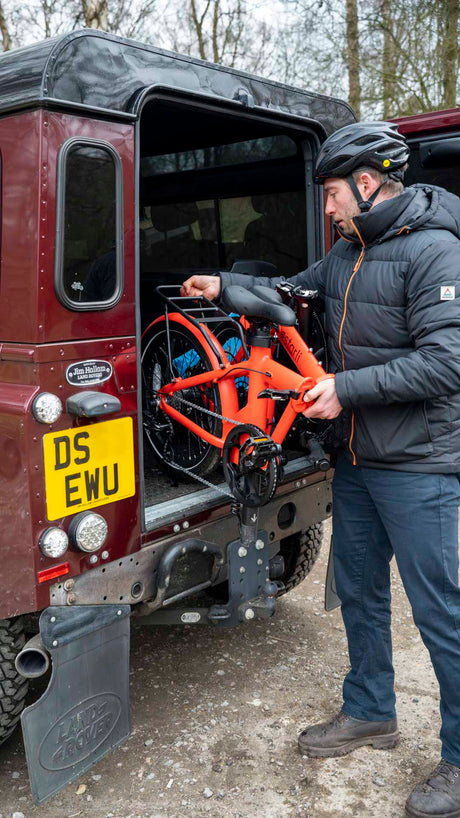 Man loading folded orange estarli E20.7 Comfort Hybrid E-Bike into SUV, highlighting its compact portability for travel and storage.