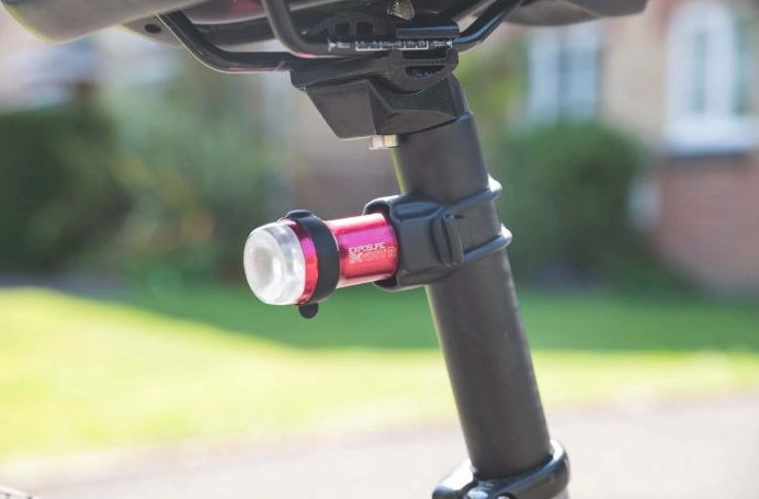 Close-up of a bike light attached to a bicycle frame with a blurred outdoor background.