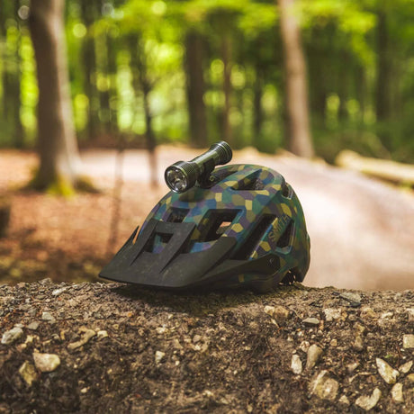 Camouflage helmet with a flashlight on a log in a forest setting