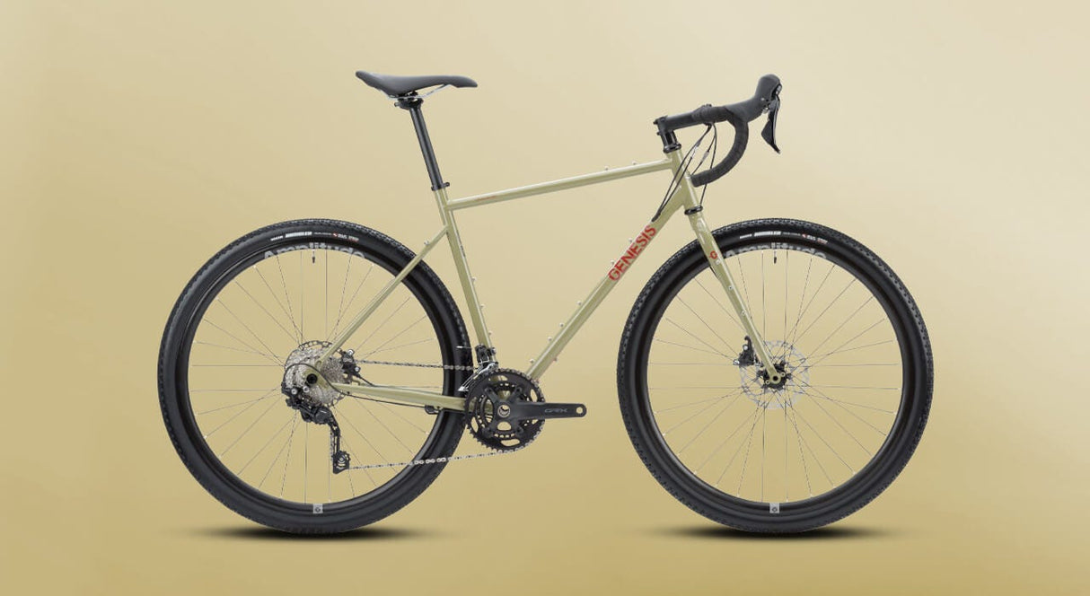 Studio shot of the 2025 Genesis Croix De Fer 30 Gravel Bike against a beige background, highlighting its sleek and rugged design.