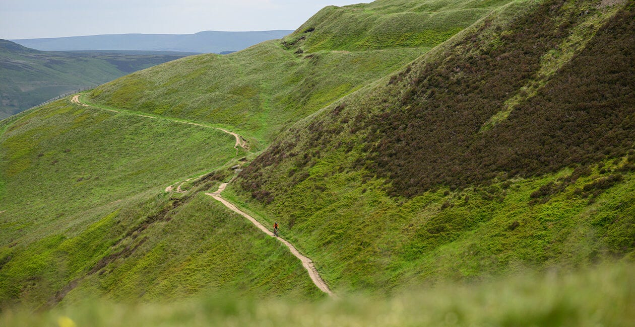 Winding gravel trail through green hills, ideal terrain for the 2025 Genesis Croix De Fer 30 Gravel Bike's adventure capabilities.