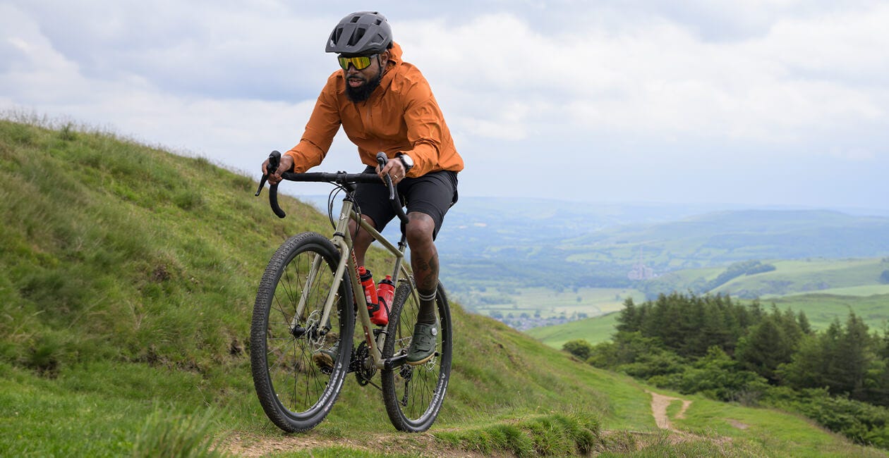 Cyclist climbing a grassy hill on the 2025 Genesis Croix De Fer 30 Gravel Bike, showcasing its endurance and off-road versatility.