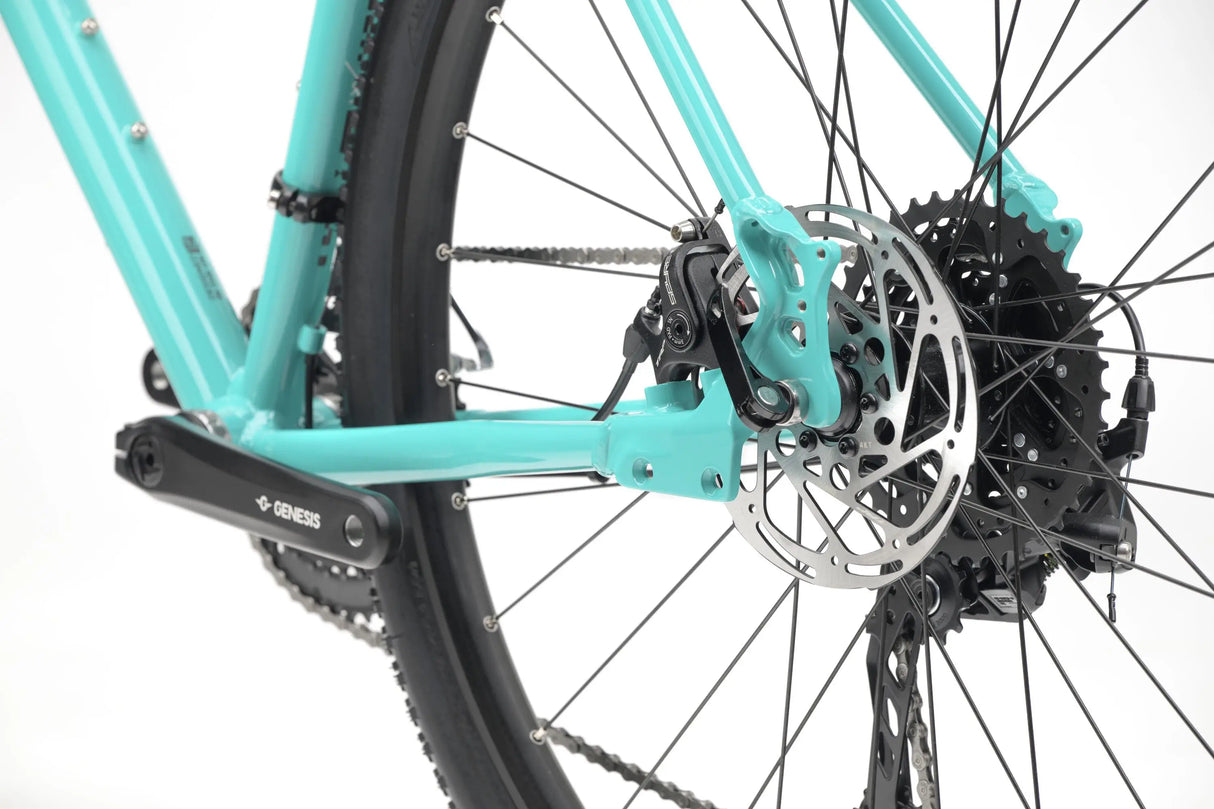 Close-up of turquoise Genesis CDA 20 gravel bike rear wheel, disc brake, and gear cassette.