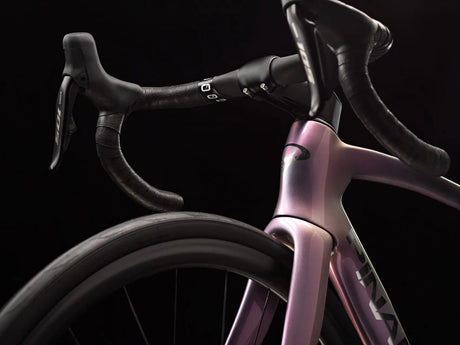 Close-up of a pink bicycle frame with black handlebars on a black background
