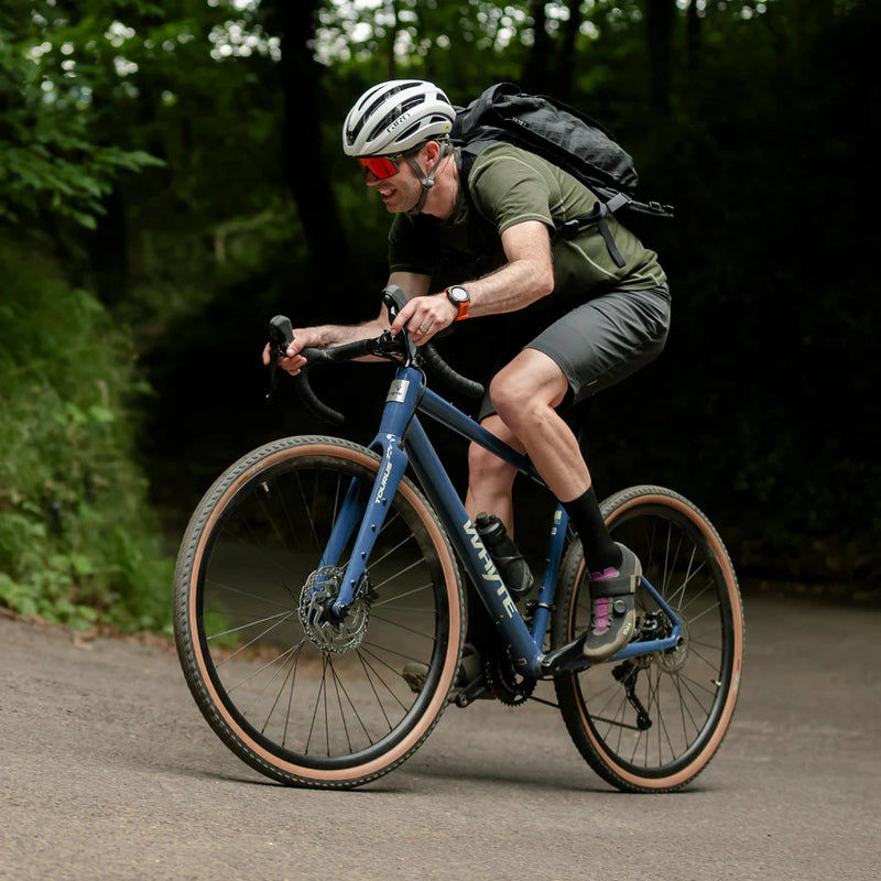 Man riding a blue bicycle on a road with greenery in the background