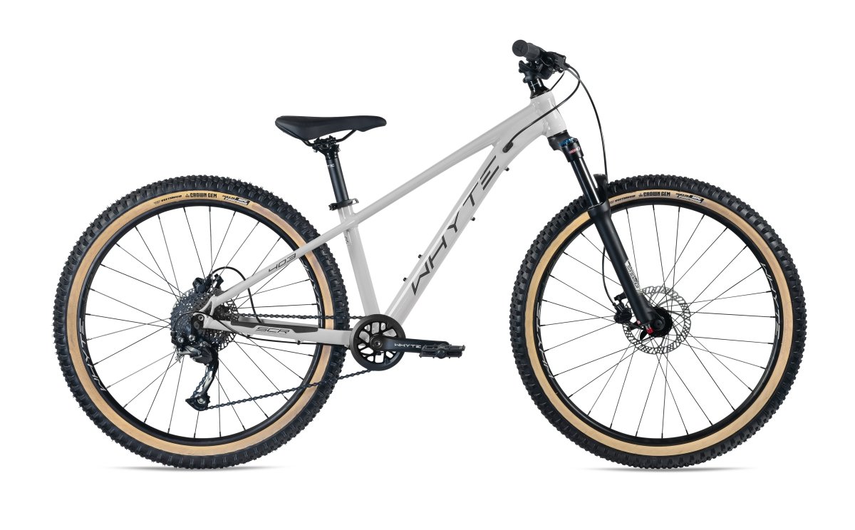 Introducing the Whyte 403 V3, a sleek mountain bike finished in a striking gloss cement color. This stylish bike boasts black handlebars, a black seat, and black tires with beige rims. It comes equipped with a front suspension fork, disc brakes, and a robust frame designed for off-road cycling.