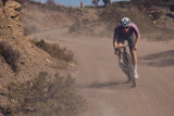 Rider riding away up a dusty gravel road on an Argon 18 Anti Matter gravel bike