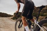 Cyclist on an Argon 18 Anti Matter gravel bike riding a dry gravel track, with scrubland and hills behind