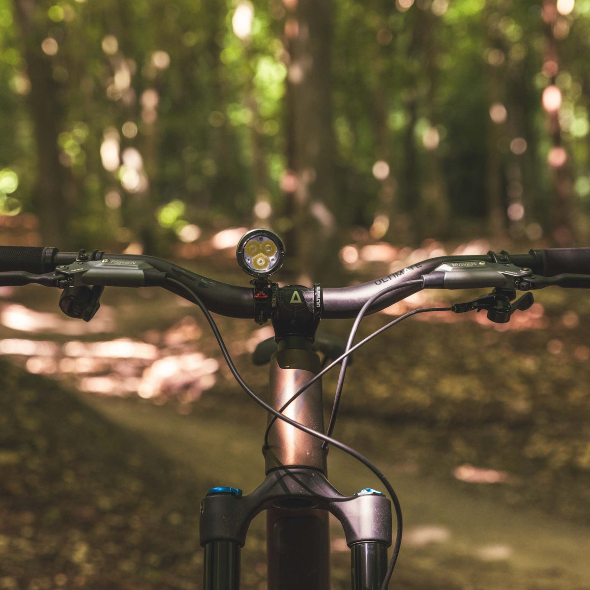 Exposure Toro Mk16 lit up on the flat bars of a mountain bike on a woodland trail