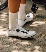 Cyclist wearing white QUOC Escape Road Shoes on a bike, demonstrating style and comfort during outdoor cycling.