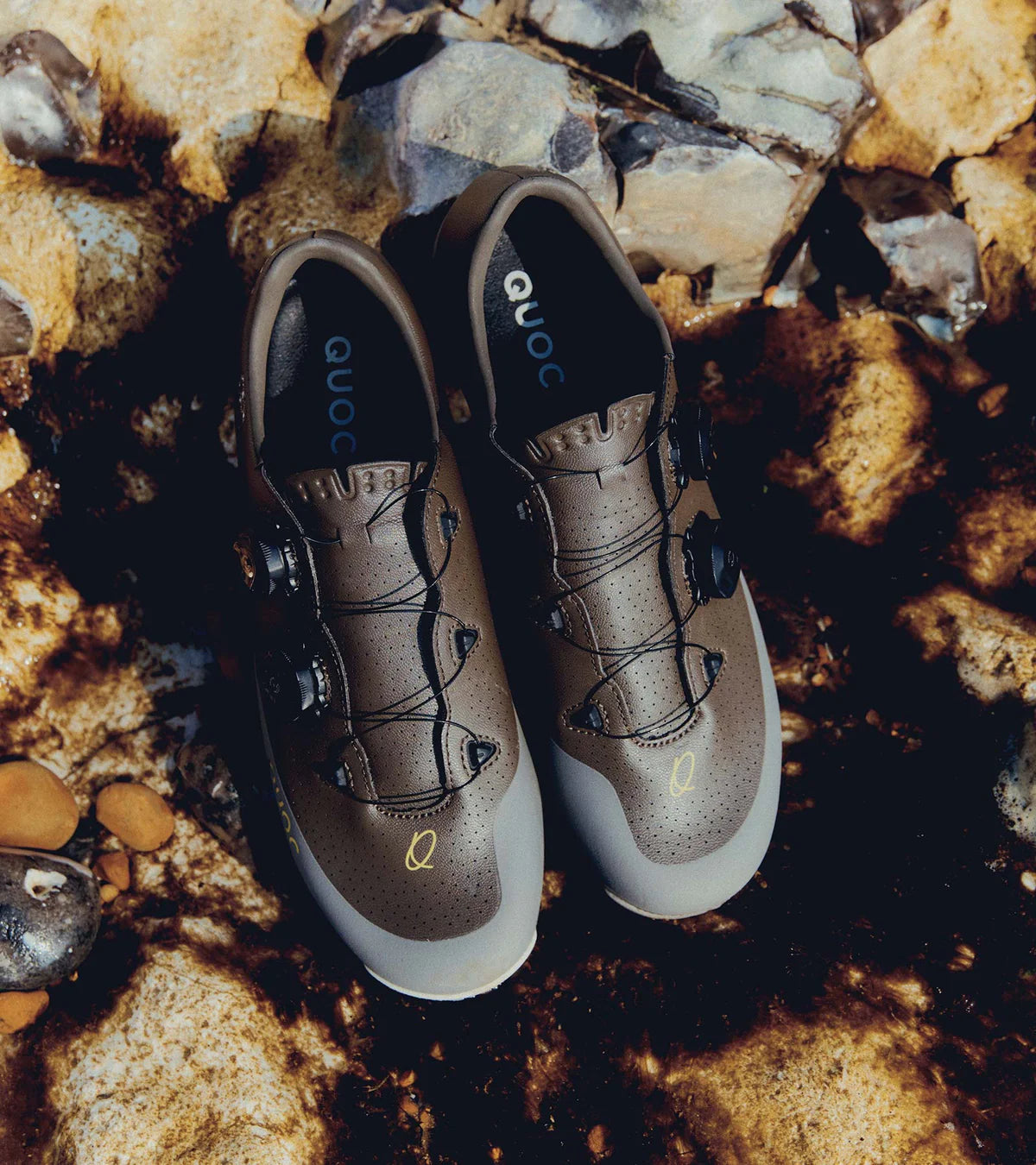 Pair of QUOC Gran Tourer XC Off-Road Shoes in brown resting on wet rocks, emphasizing their water-resistant and trail-ready build.