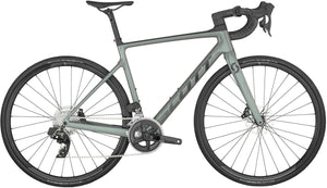 A sleek, modern road bike with a matte green frame, drop handlebars, and lightweight black tires. The bike features a high-performance gear system, disc brakes, and a minimalist design emphasizing its aerodynamic build. The brand name "Scott" is visible on the frame of the Addict 10 Green Road Bike.