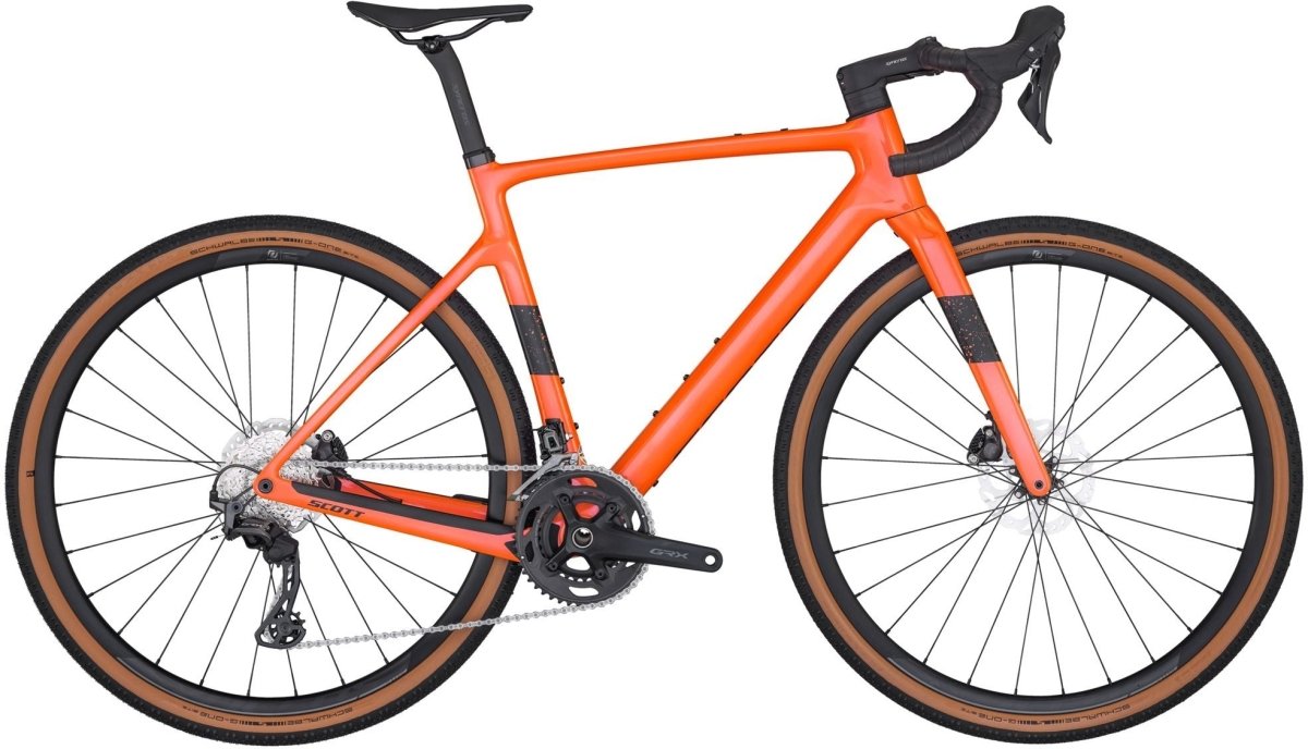 An Addict Gravel 40 from Scott, this bright orange road bike features drop handlebars, a black seat, and brown tires. Equipped with disc brakes and gear shifts, it is displayed on a white background, highlighting its sleek frame and modern design.