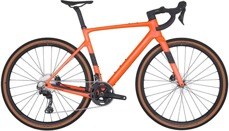 An Addict Gravel 40 from Scott, this bright orange road bike features drop handlebars, a black seat, and brown tires. Equipped with disc brakes and gear shifts, it is displayed on a white background, highlighting its sleek frame and modern design.