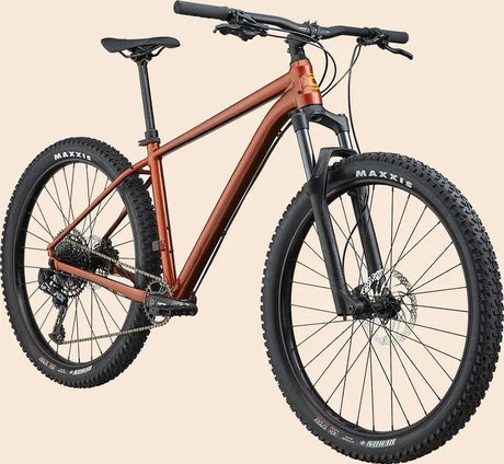 A rust-colored Cannondale Cujo 1 Kids Mountain Bike featuring thick black tires, disc brakes, and a front suspension fork. The bike boasts a sleek, modern design suitable for off-road cycling, with the brand "MAXXIS" visible on the tires.