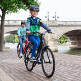 Two children on Frog City 61 Kids Hybrid Bikes ride along a riverside path, both wearing helmets and casual attire. Their lightweight frame bikes with 8-speed gears ensure a smooth journey as they pass by a stone bridge and trees, with the river gently flowing below.