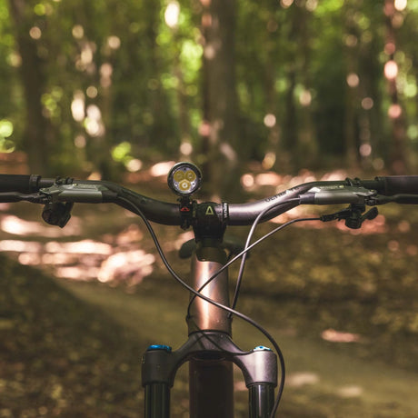 Exposure Toro Mk16 lit up on the flat bars of a mountain bike on a woodland trail