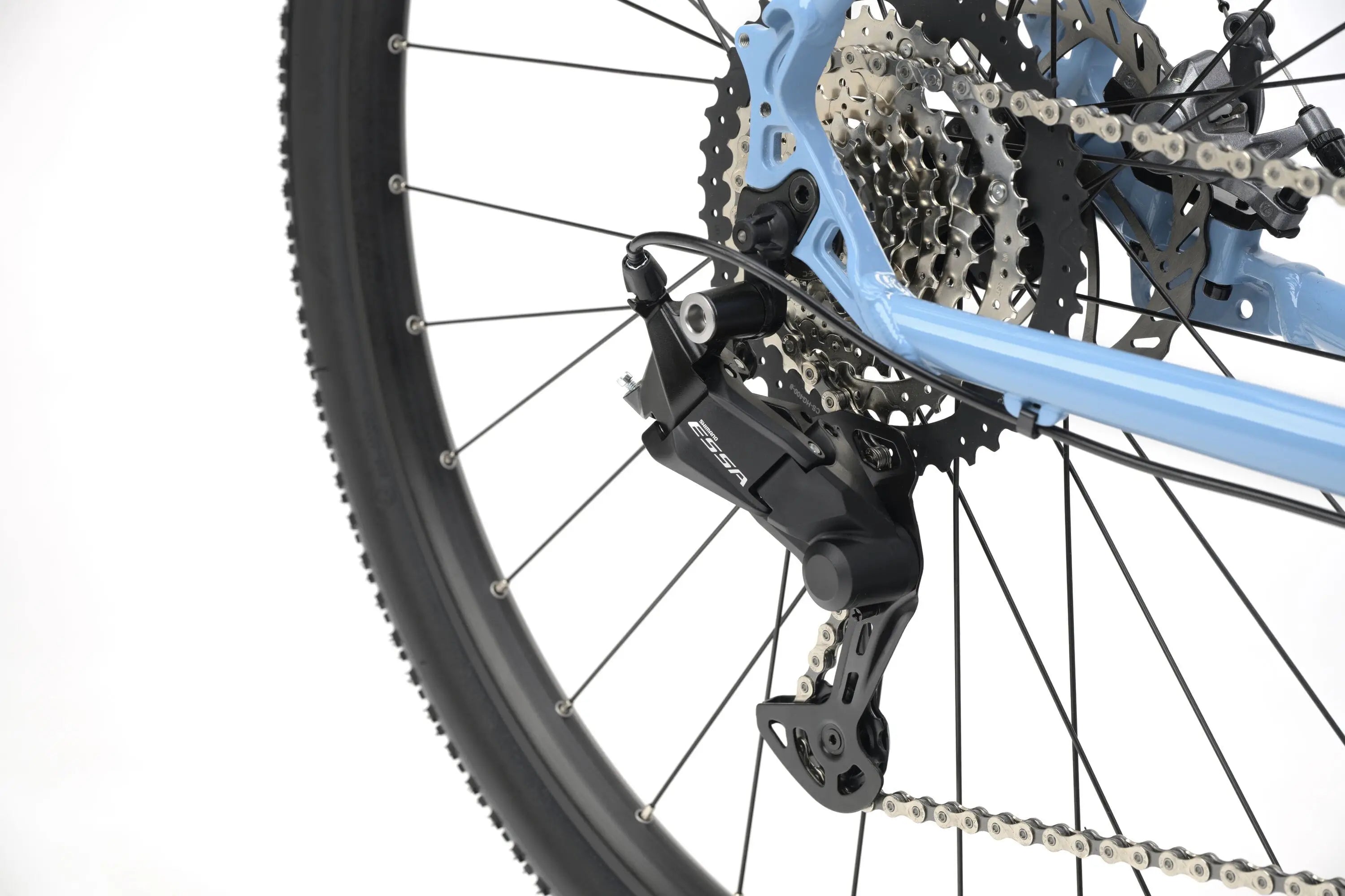 Close-up of blue gravel bike rear derailleur, cassette, and tire with knobby tread on white background.