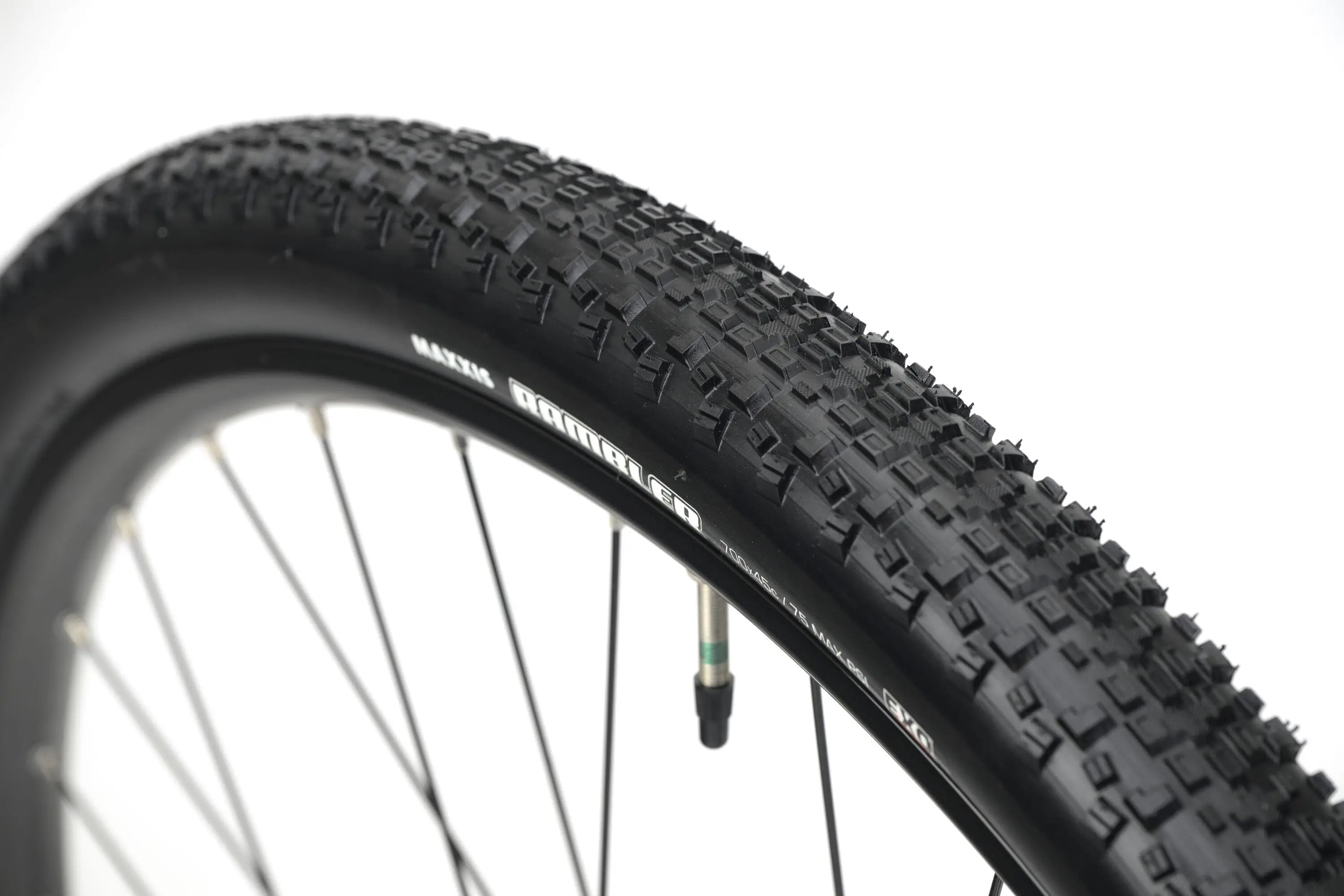 Close-up of black gravel bike tire with knobby tread pattern on metal spoke wheel.
