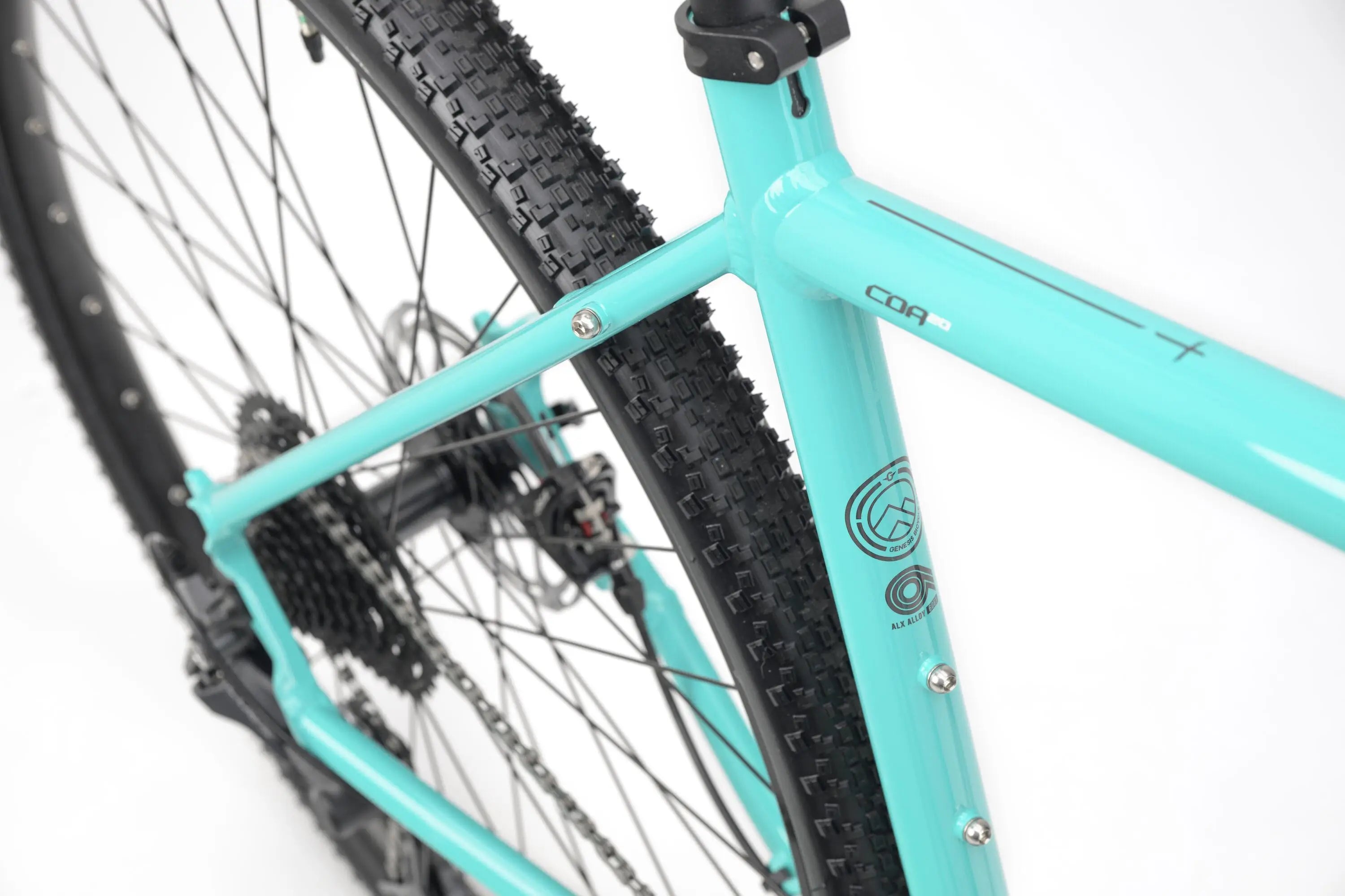 Close-up of teal Genesis CDA 20 gravel bike frame and rear tire with knobby tread and disc brake.