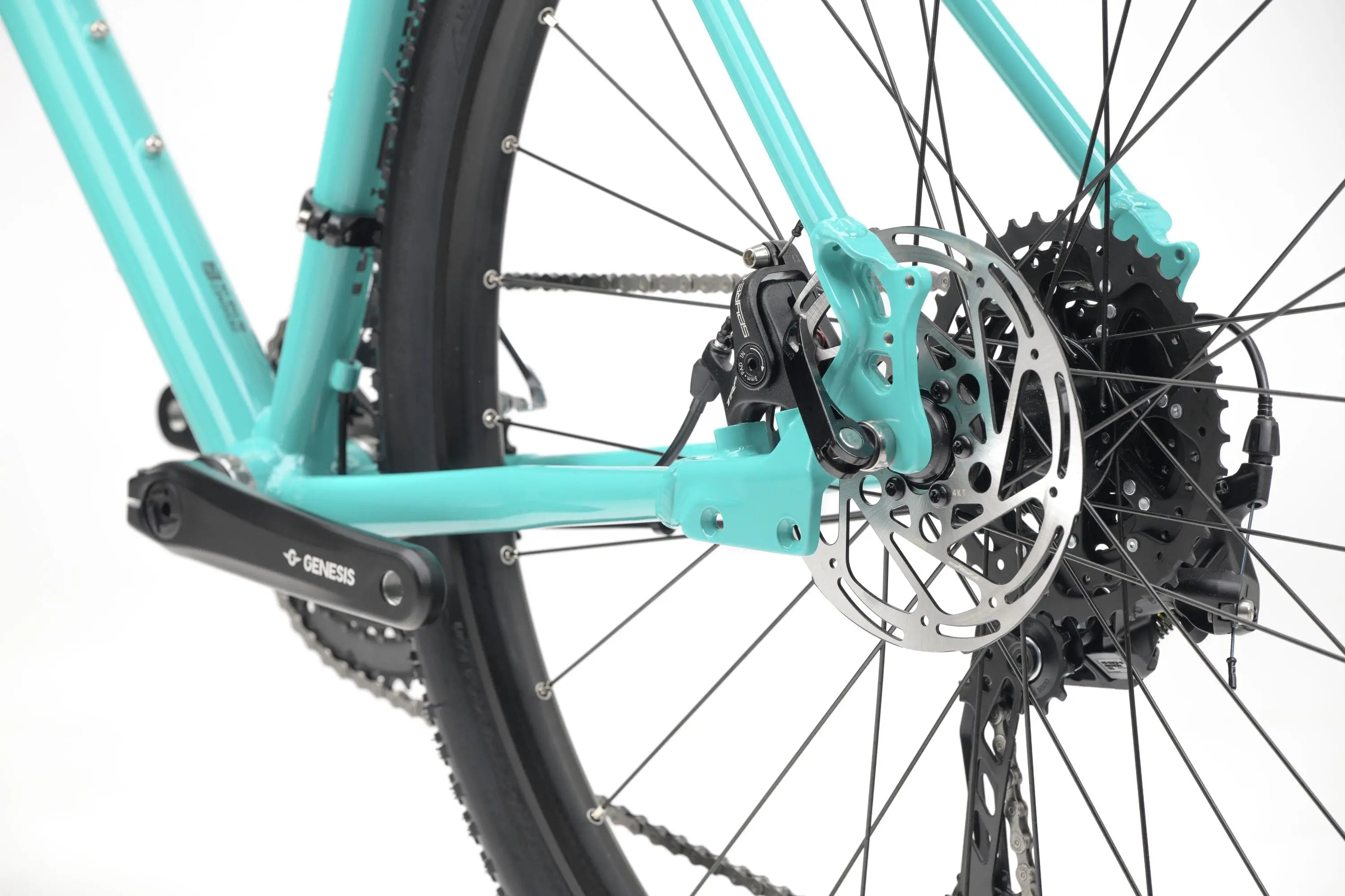 Close-up of turquoise Genesis CDA 20 gravel bike rear wheel, disc brake, and gear cassette.