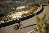 Purple and blue Merida Scultura Endurance 9000 road bike leaned forward on a winding asphalt road with guardrails.