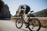 Black and blue road bike with drop handlebars ridden by cyclist on mountain road.