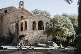 Rider on a Merida Mission 7000 gravel bike passing an old stone chapel