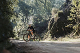 Rider on a Merida Mission 7000 gravel bike on a track through sunlit woodland