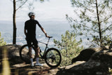 Rider standing astride a Merida Mission 7000 gravel bike at a hilltop viewpoint
