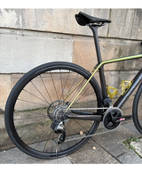 Black and gold carbon Cervelo R5 Rival AXS road bike frame with rear wheel and electronic derailleur against stone wall.